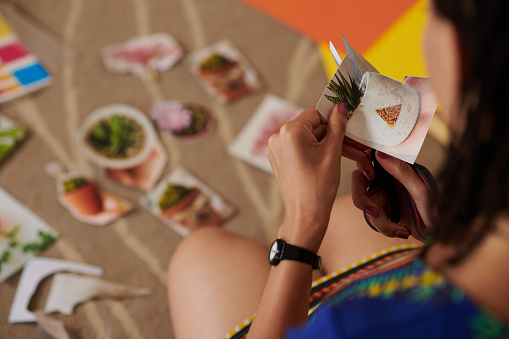 Close-up image of woman cutting out pictures of plants for collage