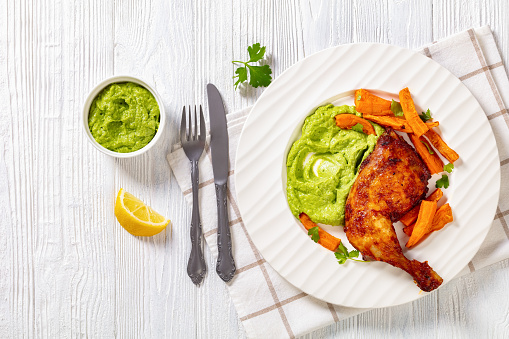 garlic chicken with guasacaca sauce of avocado, green pepper and herbs and sweet potato chips on white plate on wooden table, horizontal view from above, flat lay, free space