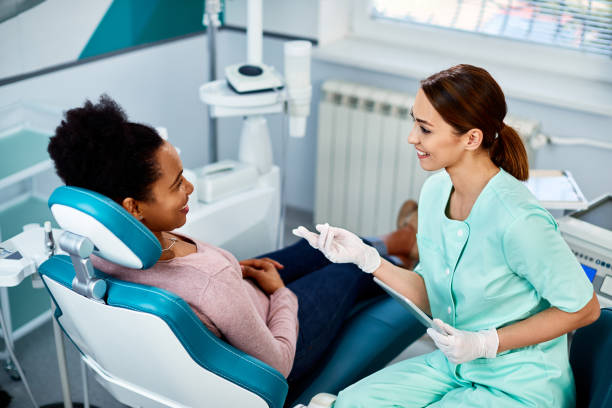 glückliche zahnärztin und ihre schwarze patientin, die in der zahnklinik spricht. - zahnarztpraxis stock-fotos und bilder