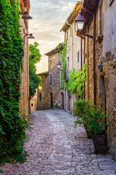 Photo of Picturesque alley with stone houses and cobblestone floor, plants and vines at golden sunset, Peratallada, Girona, Catalonia.