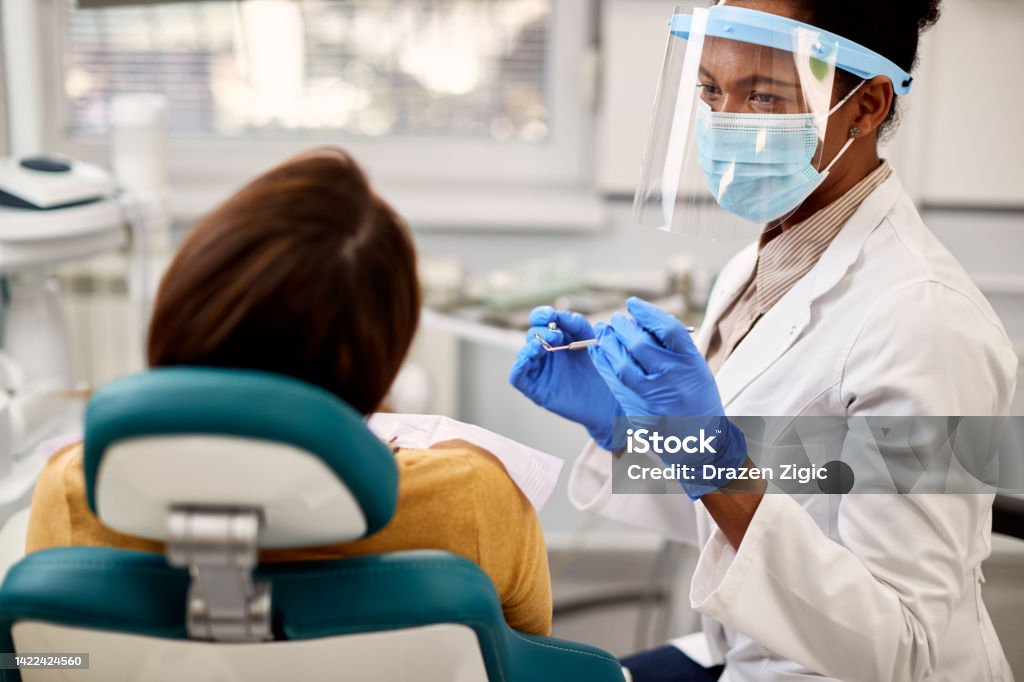 African American dentist during appointment with her patient at dental clinic. African American dentist talking to her patient during dental appointment. Dentist Stock Photo