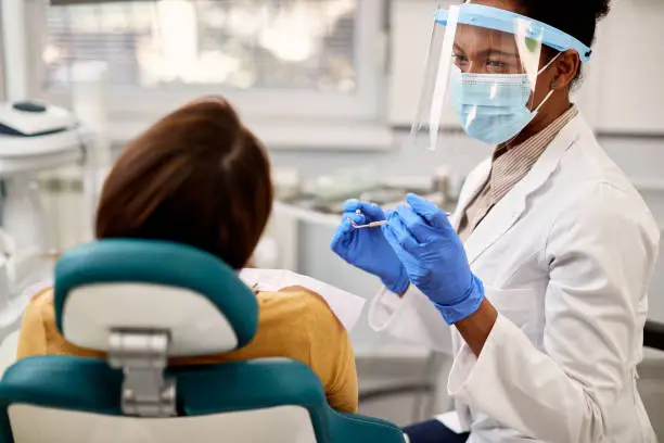 African American dentist talking to her patient during dental appointment.