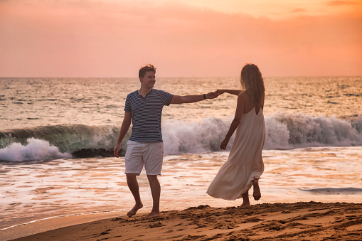 Adult lovely family couple holding hands dancing at ocean sunset background. Man and woman in casual clothes, walking together sandy beach outdoor. Travel vacation concept. Copy text space