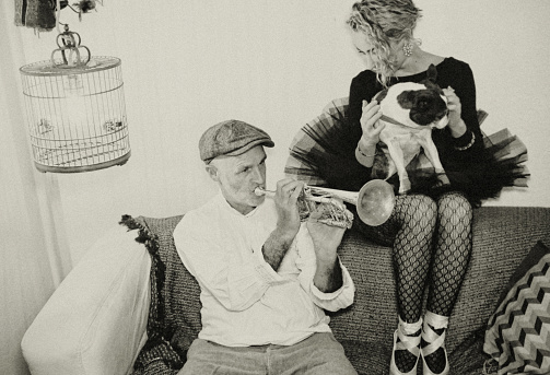 A dog, a circus musician and a ballerina sit together on a sofa.