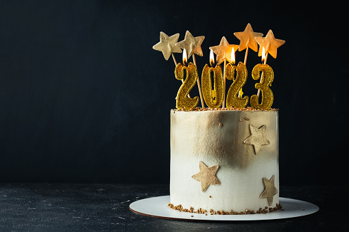Big golden New Year cake decorated with golden stars and candles against black background. Happy New Year 2023. Winter holiday background