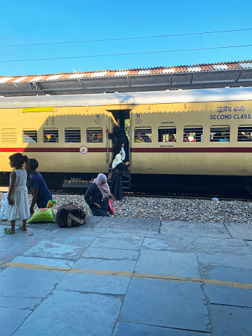 Bijnor, Uttar Pradesh, India - August 12, 2022: Stock photo showing departing train passengers 
leaving a second class train carriage to walk across rail track gravel to climb on platform of Bijnor railway station.