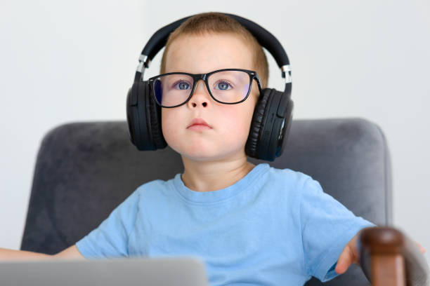 A boy in glasses and headphones listens in headphones while sitting A boy in glasses and headphones listens in headphones while sitting in an armchair and looks straight ahead. The child listens to music, a lesson or watches a cartoon. High quality photo concentrated solar power stock pictures, royalty-free photos & images