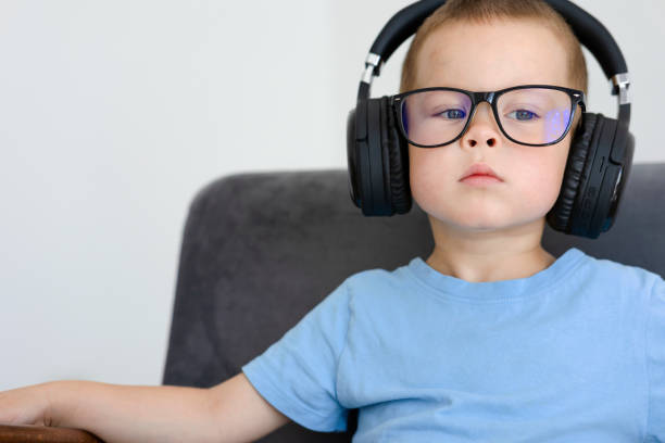 Portrait of a child in a blue T-shirt, glasses and headphones. Portrait of a child in a blue T-shirt, glasses and headphones. The boy listens to sounds in headphones while sitting in a chair very carefully with a thoughtful expression on his face. High quality photo concentrated solar power photos stock pictures, royalty-free photos & images