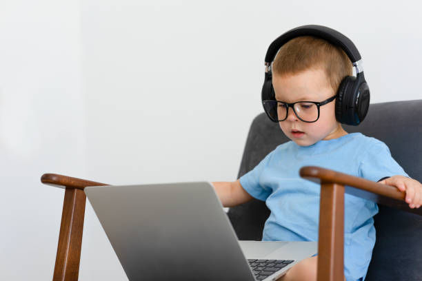 A child in a blue T-shirt with a laptop and headphones. A child in a blue T-shirt with a laptop and headphones. The child sits in an easy chair with headphones, watches a movie with a laptop or learns online. High quality photo concentrated solar power stock pictures, royalty-free photos & images