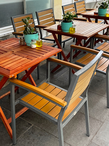 Stock photo showing close-up view of some metal and wood tables and chairs pictured outside a pavement cafe.