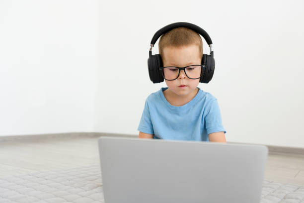The child looks at the laptop, studies or talks. The child looks at the laptop, studies or talks. A boy in a blue T-shirt and black headphones sits in front of a laptop screen and looks into it. High quality photo concentrated solar power stock pictures, royalty-free photos & images