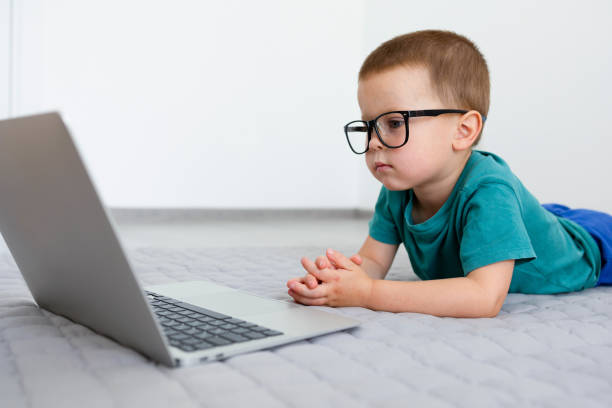 The child, looking at the laptop, learns lessons or communicates. The child, looking at the laptop, learns lessons or communicates. Little boy with a laptop. The child is watching cartoons, films or educational programs with concentration. High quality photo concentrated solar power photos stock pictures, royalty-free photos & images