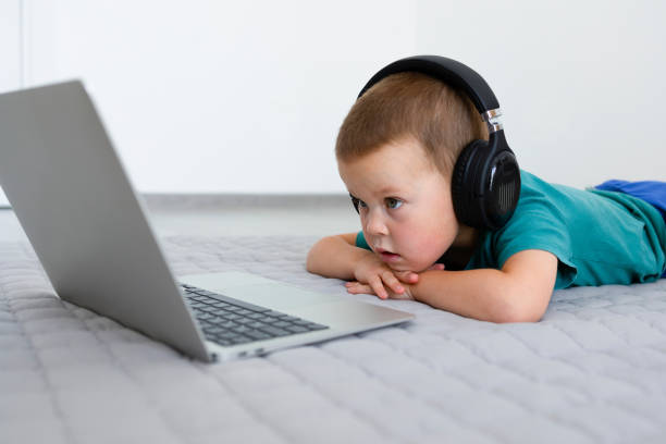A little boy in headphones is lying down watching cartoons A little boy in headphones is lying down watching cartoons or educational programs in a laptop. Education, laptop, headphones, learning new things, entertainment. High quality photo concentrated solar power stock pictures, royalty-free photos & images