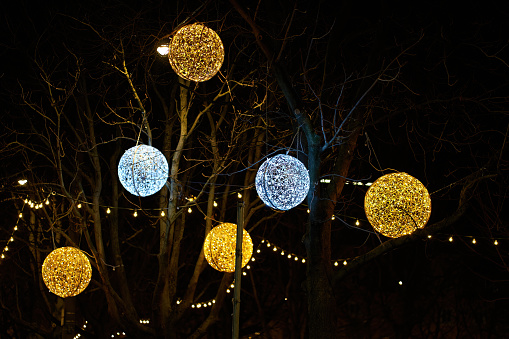 Christmas decorated tree in the city. Large illuminated baubles in silver and gold hang from the branches. In the night.