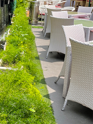 Stock photo showing close-up view of rows of rattan and glass topped patio tables surrounded by rattan wickerwork chairs pictured outside on a paved stone patio.