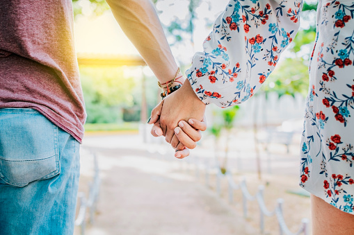 Close up of couple holding hands outdoors, Close up of young couple walking holding hands. Close-up of teenagers holding hands in a park. View of young couple holding hands outdoors