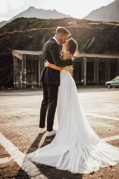 Wedding in the mountains. Full-length portrait of groom kissing and embracing the bride. White dress. Beautiful for lifestyle design. stock photo