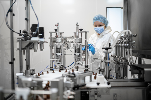 Small brown bottles seen perfectly arranged in a laboratory during manufacturing in a pharmaceutical factory while employee is controlling the process.