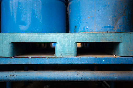 Close-up at plastic pallet with metal chemical barrels at the factory storage. Industrial equipment object photo, selective focus.