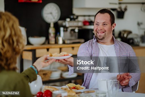 istock Portrait of happy young man with Down syndrome with his mother at home having breakfast together. 1422452162