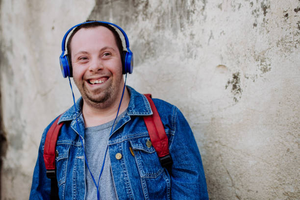 Close-up portrait of happy young man with Down sydrome listening to music when walking in street. stock photo