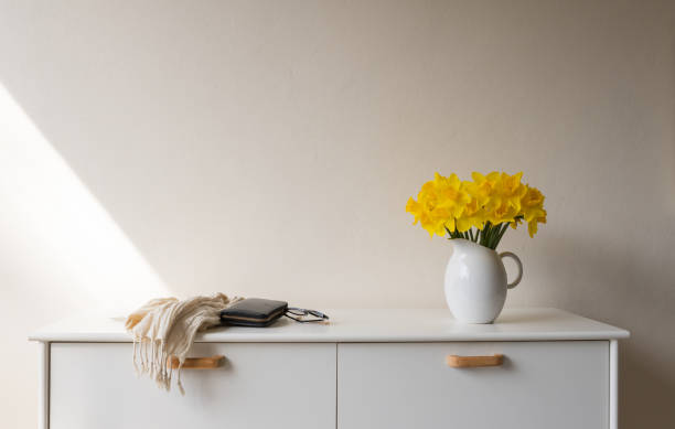 желтые нарциссы в белом кувшине на боковом столике рядом с шарфом, сумочкой и бокалами - daffodil flower yellow vase стоковые фото и изображения