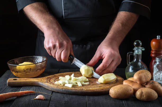 istock Professional chef cuts raw potatoes into pieces with a knife before preparing breakfast or dinner. Close-up of a cook hands while working in a restaurant kitchen 1422453979