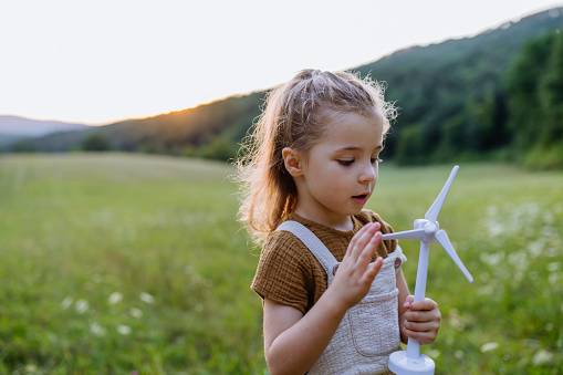 A little girl standing in nature with model of wind turbine. Concept of ecology future and renewable resources.