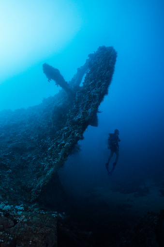 Silhouette of a scuba diver swimming next to the giant propeller of an old ship wreck