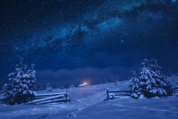 Lonely house on a snowy hill with Christmas light Bright milky way in a night starry sky. Lonely house on a snowy hill with Christmas light. fairy tale village stock pictures, royalty-free photos & images