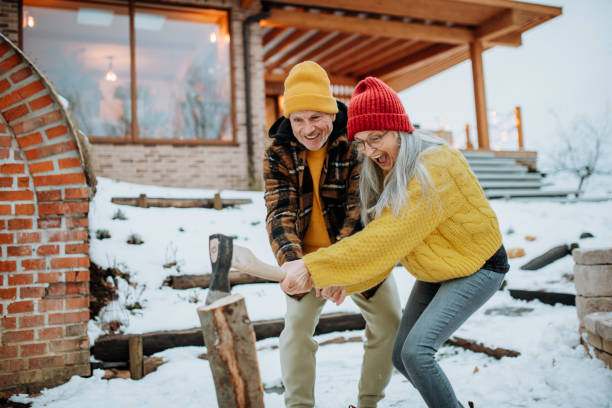 Senior couple chopping wood together in front of their house, during cold winter day. stock photo