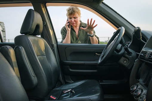 Middle-aged woman looks through the glass into the interior of her car with the keys in the driver's seat. Woman driver forgot her keys in the car and calling technical assistance