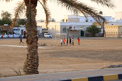 March 21 2022 - Sur in Oman: children playing soccer in a dirt field in front of mosque in the city of Sur