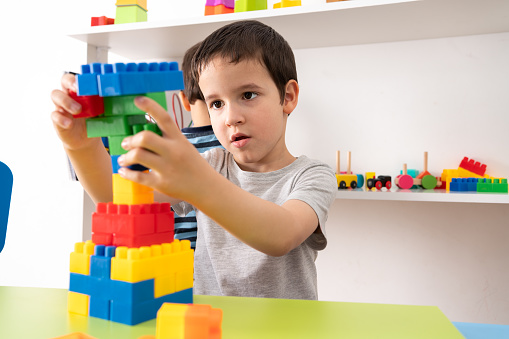 Little boy playing with colourful educational toy blocks on the table at preschool or kindergarten. Kid having fun while engaged in creative learning and development