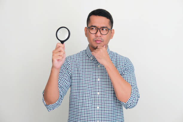 istock Asian man holding magnifying glass with curious face expression 1422476153
