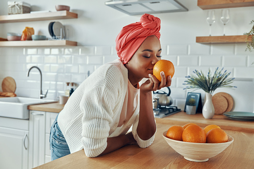 Hermosa mujer africana con sombreros tradicionales que huelen a naranjas mientras está de pie en la cocina photo