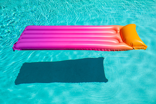 Bright pink inflatable sun bed floating with a shadow in turquoise pool in Palm Springs