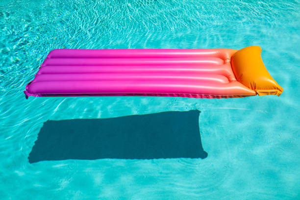 Bright pink inflatable sun bed floating in turquoise pool stock photo