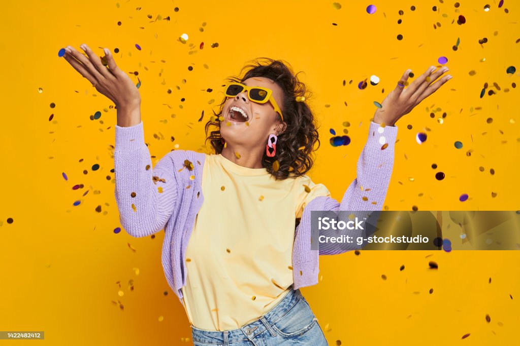 Beautiful African woman throwing confetti and smiling against yellow background Eyeglasses Stock Photo