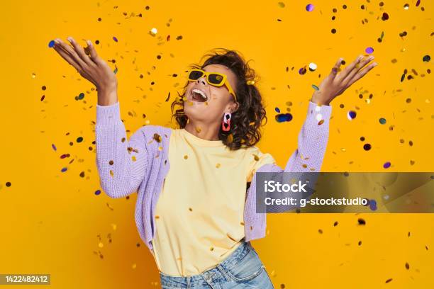Beautiful African Woman Throwing Confetti And Smiling Against Yellow Background Stock Photo - Download Image Now