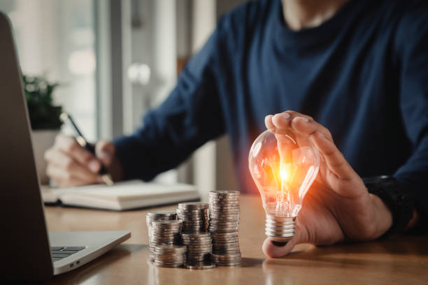 istock Businessman holding and putting lightbulb on coins stack on table for saving energy and saving money concept. 1422486839