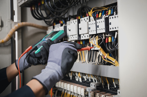 Servicio de electricidad y mantenimiento eléctrico, ingeniero de mano sosteniendo el multímetro de CA que verifica el voltaje de corriente eléctrica en el terminal del disyuntor y el cableado del cable de la placa de distribución de energía principal. photo