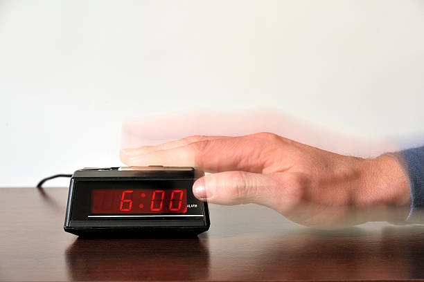 Alarm clock stopped at six o'clock alarm set at six, snooze button pushed by hand. The clock is in focus and the hand is in blurred motion. alarm clock snooze stock pictures, royalty-free photos & images