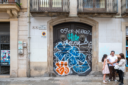 Barcelona, Spain - July 7, 2022: A man, woman and girl standing near a door with graffiti. The door is on an exterior wall of an apartment building.