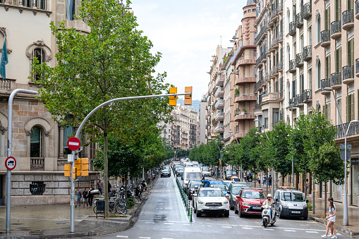 Barcelona, Spain - July 7, 2022: People crossing a zebra crossing on a sunny day in the city. Vehicles wait for the people to cross the zebra crossing and incidental people are walking on the street.