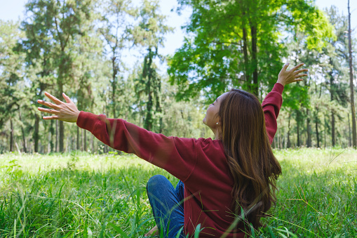 Portrait image of a beautiful young woman raising hands while sitting and relaxing in the park