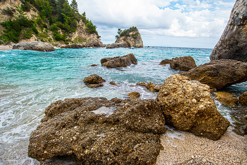 Exotic beach near Parga with sandy and pebbles beach and a big rock in the blue sea, in a pine trees forest. Background view of horizon and blue sky