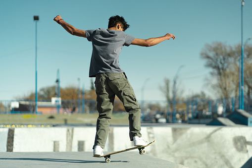Latin American skater boy doing trick in profile at the skate park.