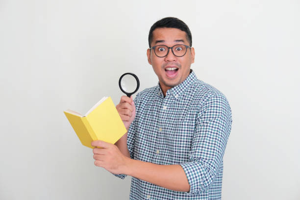 istock Asian man holding magnifying glass and book with wow expression 1422507943
