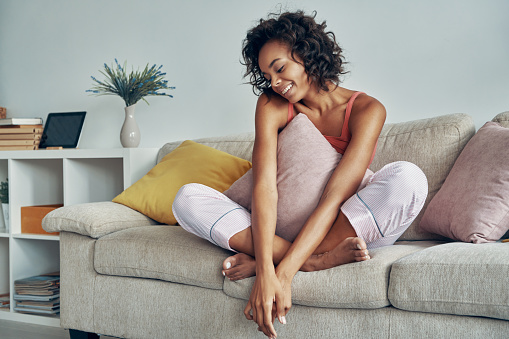 Beautiful young African woman smiling while relaxing on the couch at home